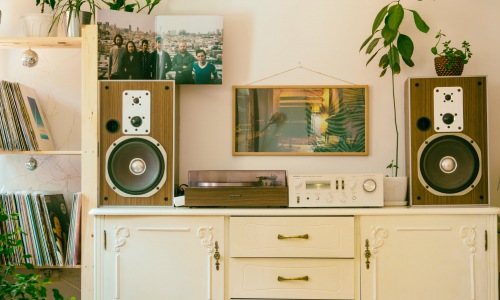 Stereo speakers and record player sitting on top of an old white dresser. Next to the dresser is a shelf full of records and plants